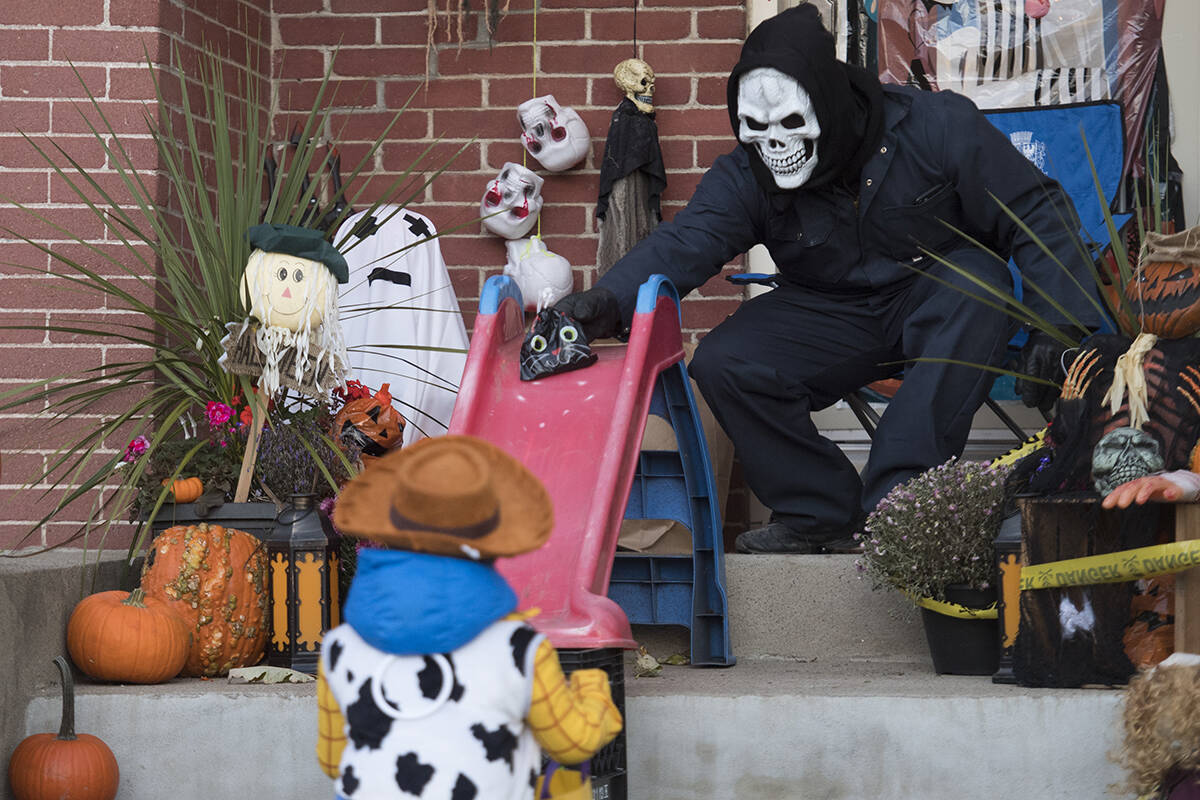 FILE – Alessandro Priolo slides a bag of candy to a young boy at his house on Halloween in Montreal, Saturday, October 31, 2020, as the COVID-19 pandemic continues in Canada and around the world. THE CANADIAN PRESS/Graham Hughes