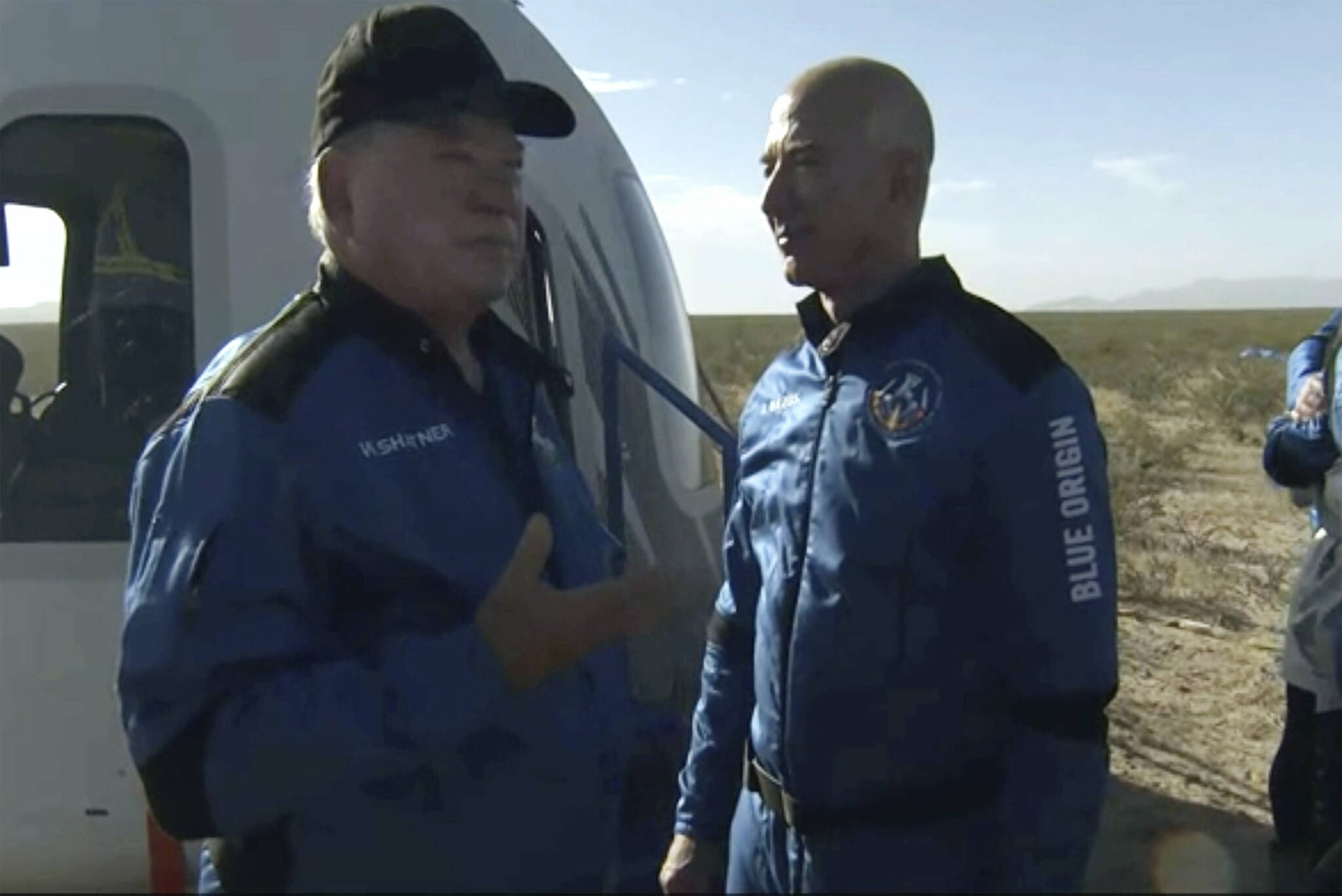 In this image provided by Blue Origin, William Shatner talks with Jeff Bezos about his experience after exiting the Blue Origin capsule near Van Horn, Texas, Wednesday, Oct. 13, 2021.  The “Star Trek” actor and three fellow passengers hurtled to an altitude of 66.5 miles (107 kilometers) over the West Texas desert in the fully automated capsule, then safely parachuted back to Earth in a flight that lasted just over 10 minutes.  (Blue Origin via AP)