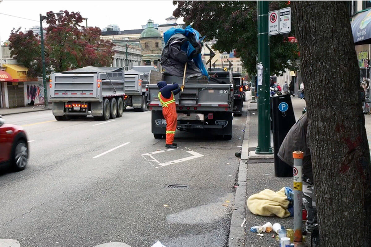 Vancouver City workers throw a tent into a garbage truck during a street sweep. (Meenakshi Mannoe/Pivot Legal Society)