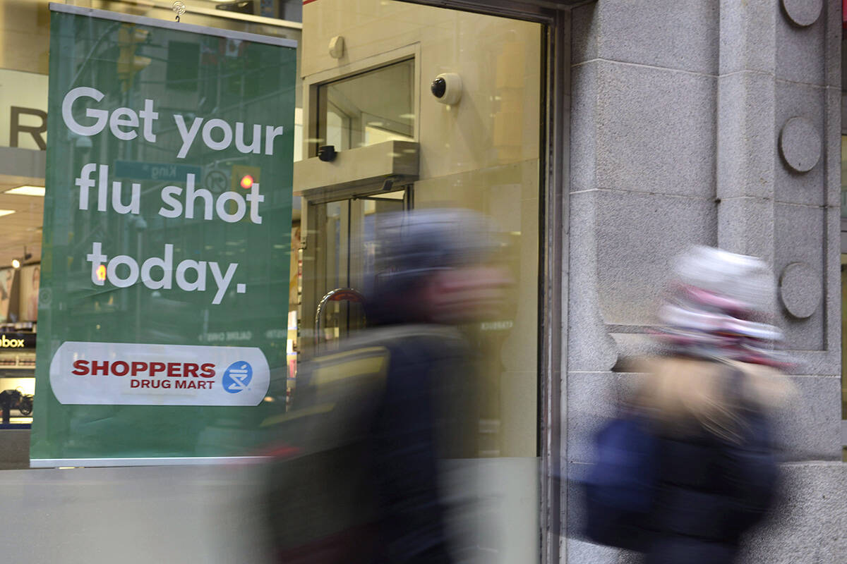 People walk pass a sign for flu shots. THE CANADIAN PRESS/Doug Ives