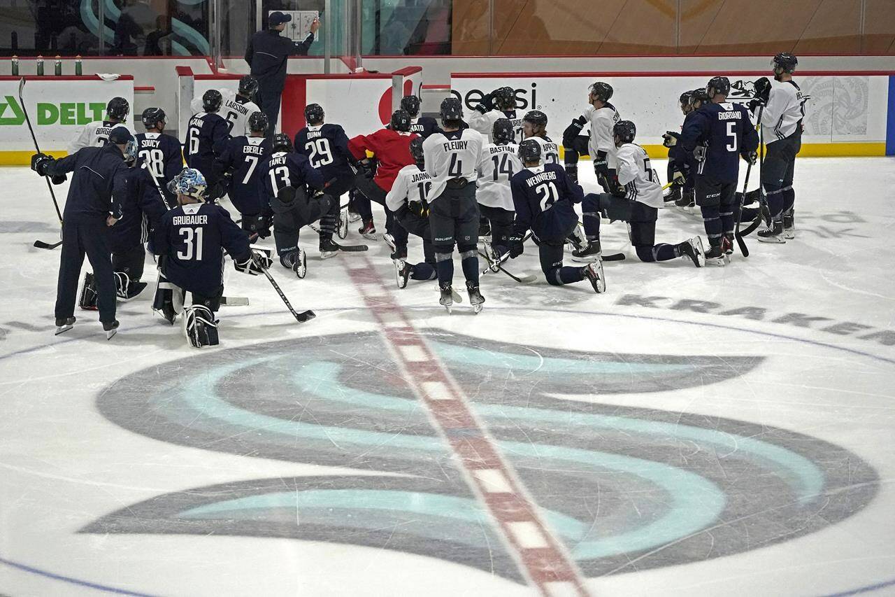 Seattle Kraken players kneel on the ice at their training facility as head coach Dave Hakstol outlines a play during NHL hockey practice, Thursday, Oct. 21, 2021, in Seattle. The Kraken will face the Vancouver Canucks, Saturday in Seattle for the expansion team’s home opener. (AP Photo/Ted S. Warren)