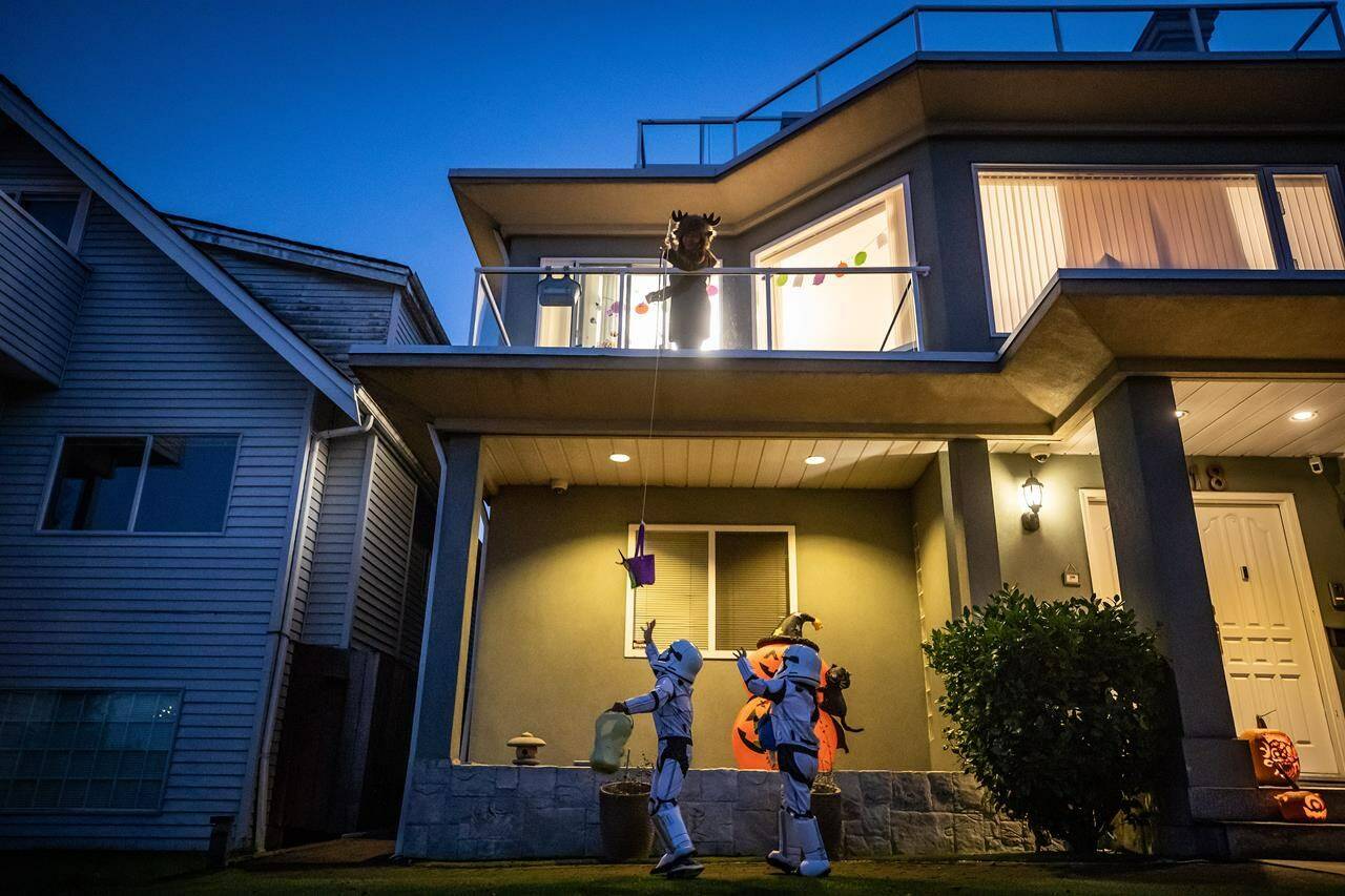 Delia Chang uses bamboo and a string to lower candy down to trick-or-treaters at her home on Halloween amid the COVID-19 pandemic, in Vancouver, B.C., Saturday, Oct. 31, 2020. Many parents are planning to let their children go trick-or-treating this year — but they may find fewer doors open than in pre-pandemic Halloweens. THE CANADIAN PRESS/Darryl Dyck