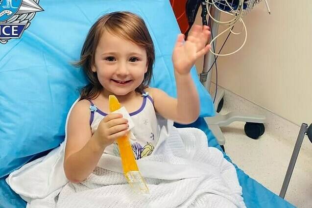 In this photo provided by the Western Australia Police, four-year-old Cleo Smith waves as she sits on a bed in hospital, Wednesday, Nov. 3, 2021, in undisclosed location, Australia. Police smashed their way into a suburban house on Wednesday and rescued Cleo whose disappearance from her family’s camping tent on Australia’s remote west coast more than two weeks ago both horrified and captivated the nation. The seal of Western Australia Police is seen at top left. (Western Australia Police via AP)
