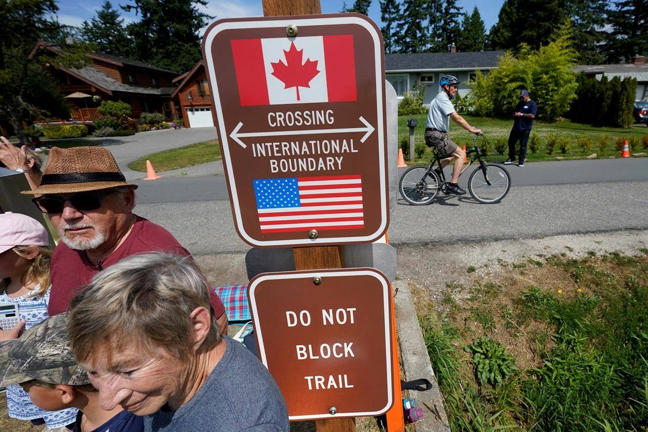 A family visits across the U.S.-Canada border at the Peace Arch Historical State Park as a cyclist rides past on the Canadian side, Monday, Aug. 9, 2021, in Blaine, Wash. THE CANADIAN PRESS/AP-Elaine Thompson