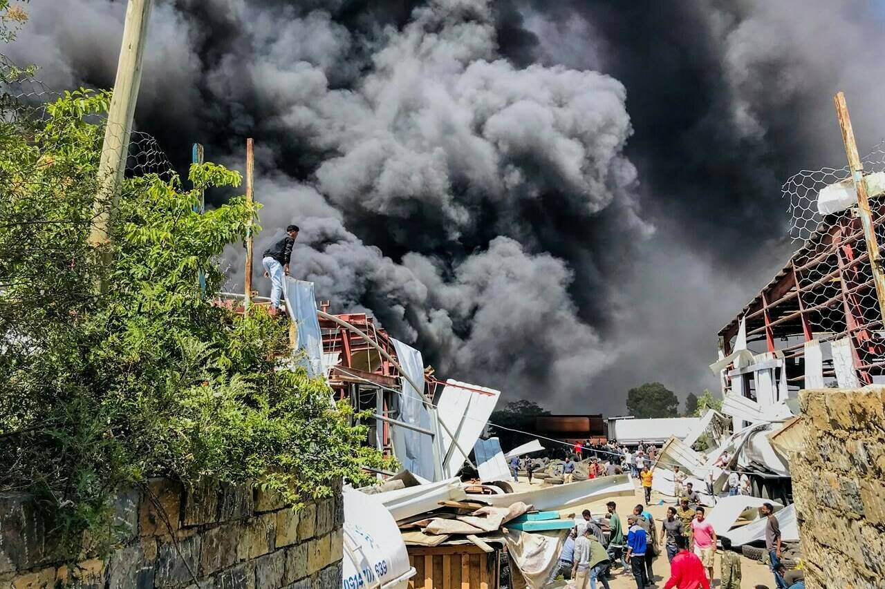 People are seen in front of clouds of black smoke from fires in the aftermath at the scene of an airstrike in Mekele, the capital of the Tigray region of northern Ethiopia Wednesday, Oct. 20, 2021. THE CANADIAN PRESS/AP Photo