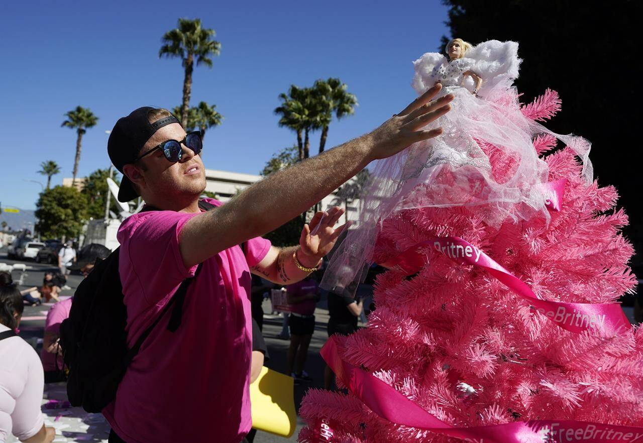 Britney Spears supporter Saige Douglas, of Denver, Col., decorates a "Free Britney" Christmas tree with a Britney Spears doll he created, outside a hearing concerning the pop singer's conservatorship at the Stanley Mosk Courthouse, Friday, Nov. 12, 2021, in Los Angeles. (AP Photo/Chris Pizzello)