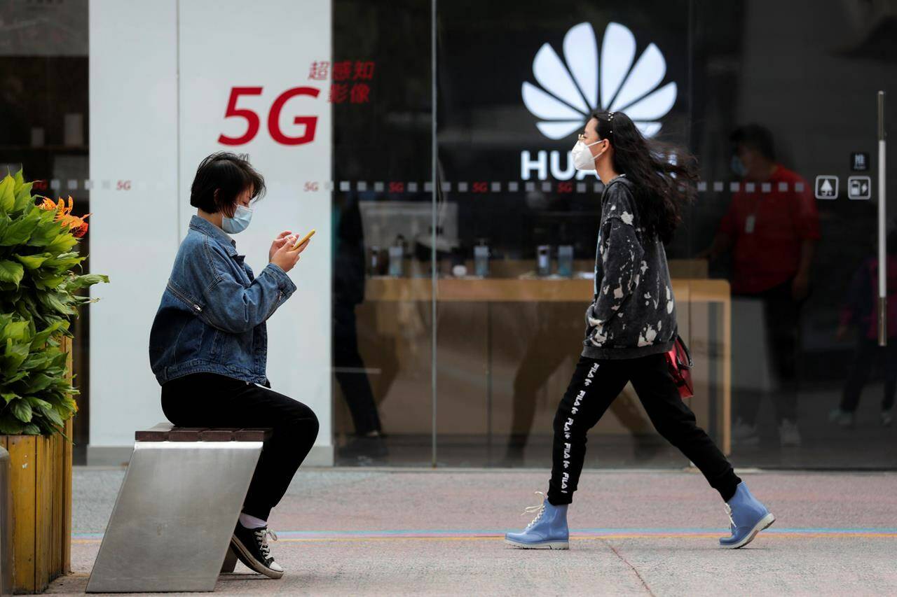 In this Oct. 11, 2020, file photo, a woman wearing a face mask to help curb the spread of the coronavirus browses her smartphone as a masked woman walks by the Huawei retail shop promoting its 5G network in Beijing. As the Liberal government prepares to unfurl its policy on next-generation mobile networks, global security experts say all signs point to the exclusion of Chinese vendor Huawei Technologies from the long-awaited blueprint. THE CANADIAN PRESS/AP, Andy Wong