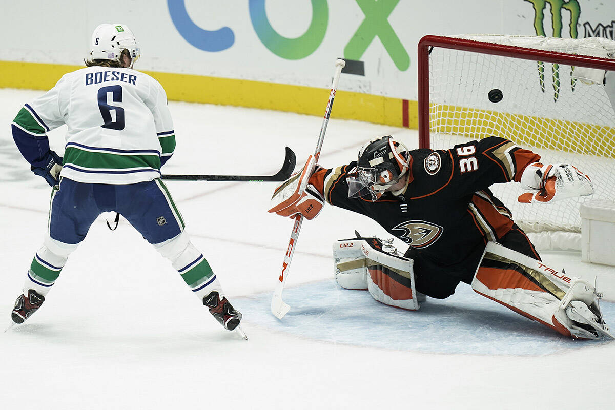 Anaheim Ducks goaltender John Gibson, right, deflects the puck hit by Vancouver Canucks’ Brock Boeser during the second period of an NHL hockey game Sunday, Nov. 14, 2021, in Anaheim, Calif. (AP Photo/Jae C. Hong)
