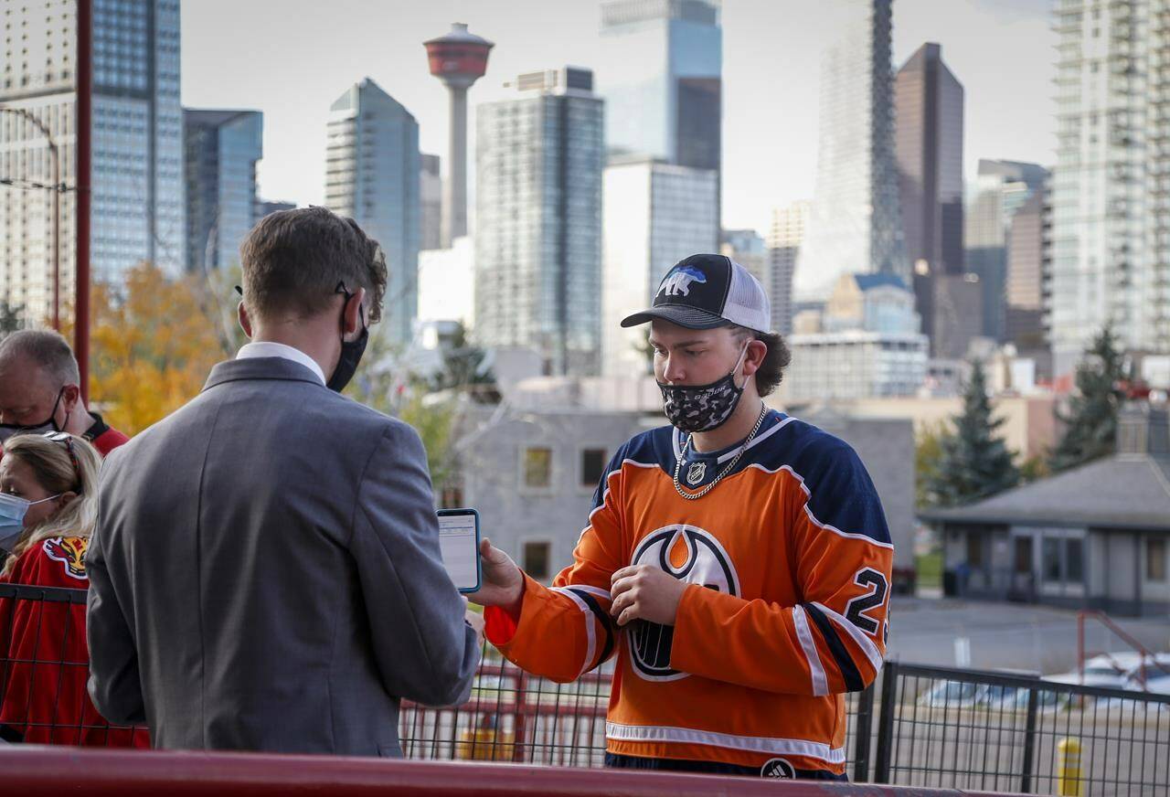 An Edmonton Oiler fan has their COVID-19 vaccination proof checked before entering the Saddledome for pre-season NHL hockey action in Calgary, Alta., Sunday, Sept. 26, 2021. Starting today in Alberta, you’re going to need more than a sheet of paper you got from a COVID-19 vaccine clinic in order to sit down at a restaurant, work out at a gym or gain entry to many venues like indoor arenas or movie theatres. THE CANADIAN PRESS/Jeff McIntosh