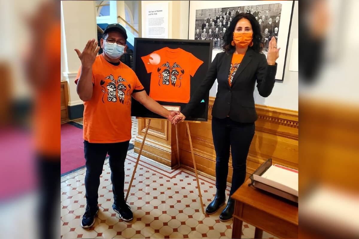 Co-founders of the Victoria chapter of Orange Shirt Day Eddy Charlie and Kristin Spray stand with a framed orange shirt featuring a design by Indigenous artist Bear Horne and a quote from Charlie. This shirt is on display in the B.C. legislature following a presentation ceremony on Oct. 27. (Photo courtesy of Kristin Spray)