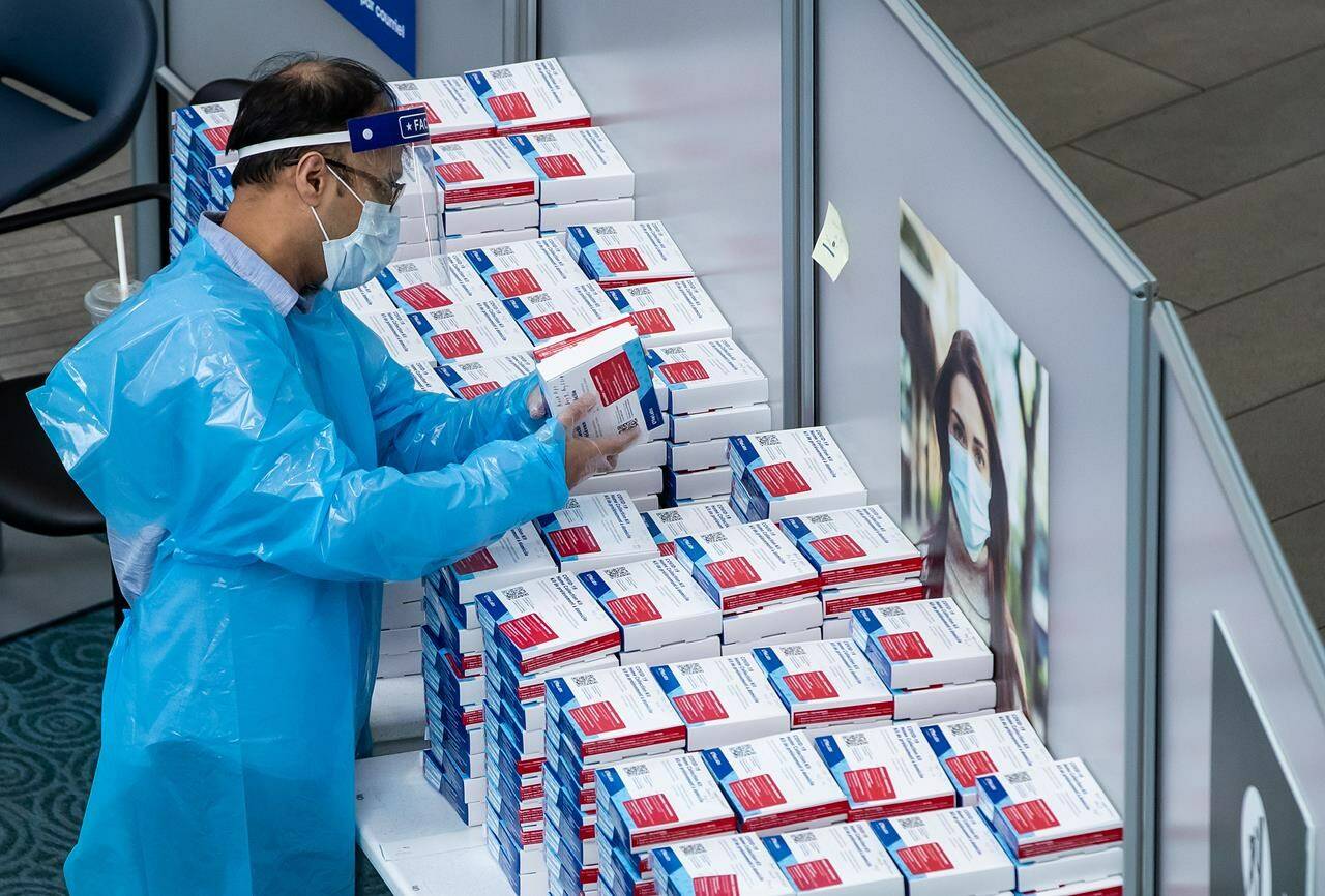 A worker picks up a COVID-19 self collection test kit which are given to arriving international passengers at Vancouver International Airport, in Richmond, B.C., Friday, July 30, 2021. THE CANADIAN PRESS/Darryl Dyck