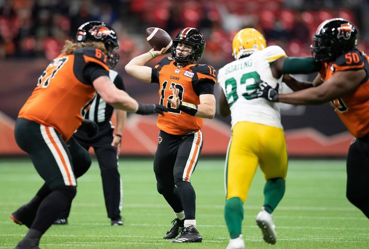 B.C. Lions quarterback Nathan Rourke (12) passes as Phillip Norman (50) holds off Edmonton Elks’ Kwaku Boateng (93) during the first half of a CFL football game in Vancouver, on Friday, November 19, 2021. THE CANADIAN PRESS/Darryl Dyck