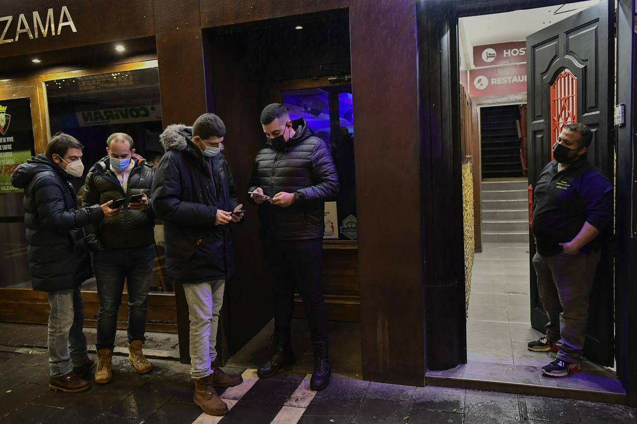 A doorman controls European passport COVID-19 to customers before the access of a bar discotheque, in Pamplona, northern Spain. Saturday, Nov. 27, 2021. Some Spanish regional communities demand from this midnight European passport COVID-19, Navarra Community one of them, in an effort to try to control the pandemic with a high curve of cases. (AP Photo/Alvaro Barrientos)