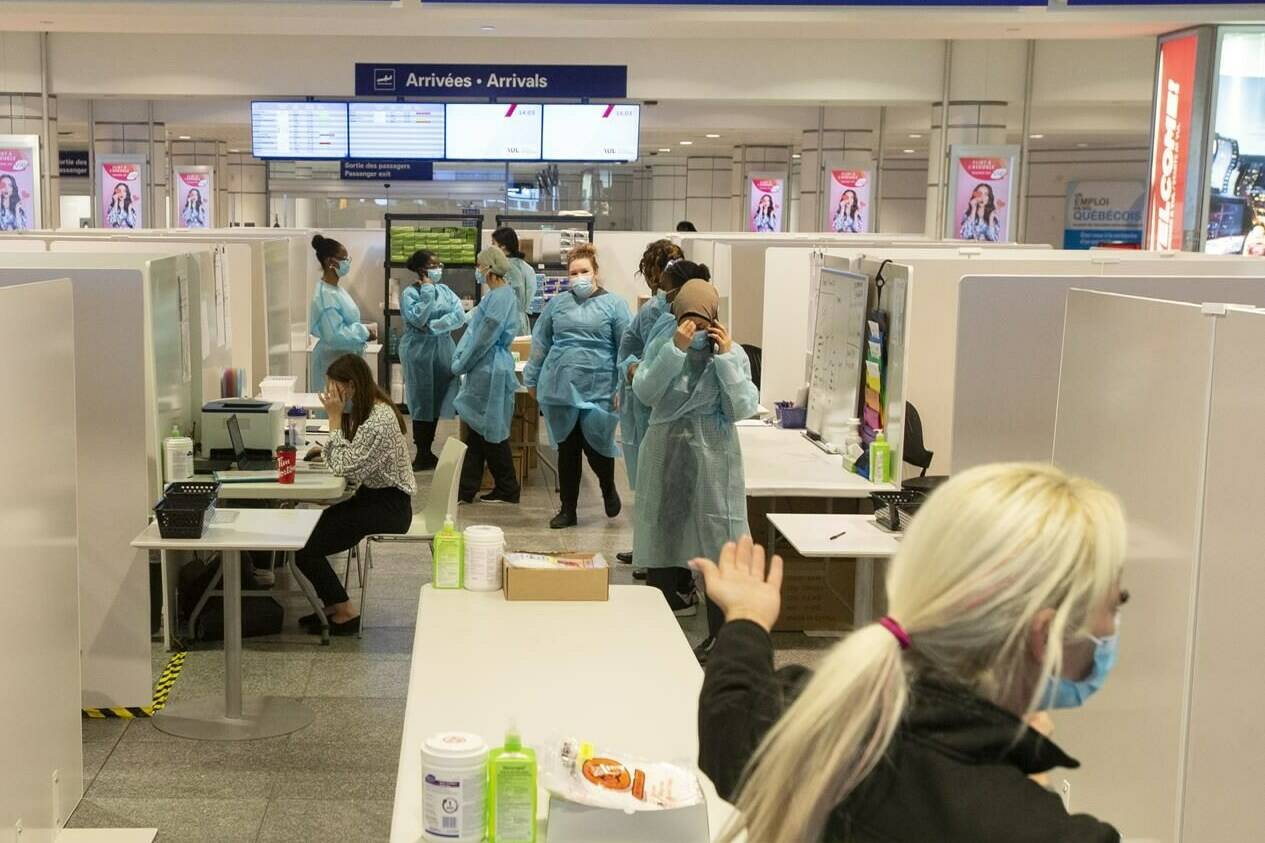 Healthcare workers wait for airline passengers at a COVID-19 testing center at Trudeau Airport in Montreal, Friday, Feb. 19, 2021. Unvaccinated travellers over the age of 12 won’t be able to board a plane or train in Canada as of today, now that the grace period has ended on the government’s COVID-19 vaccine mandate. THE CANADIAN PRESS/Ryan Remiorz