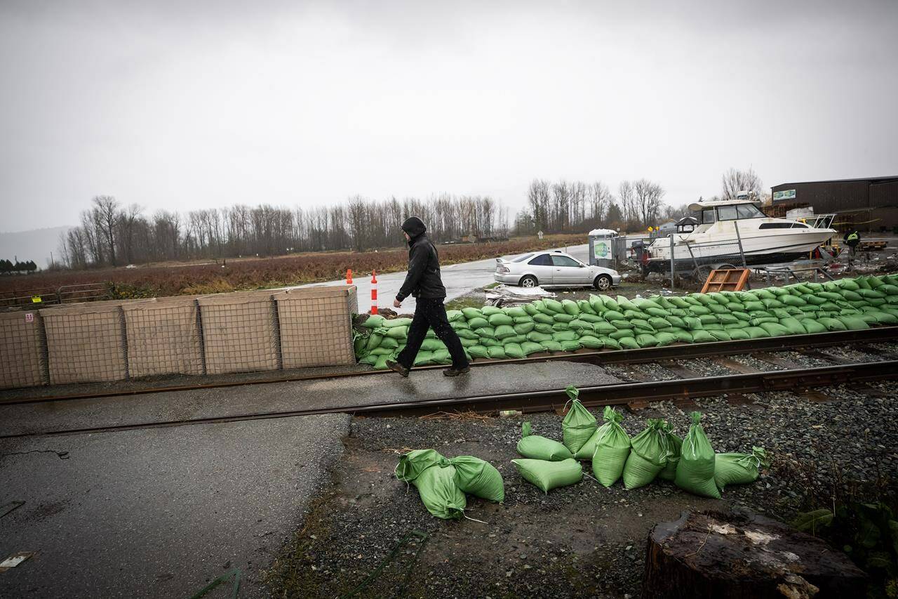 Bins of sand are placed across the road next to a wall of sandbags along rail tracks to form a temporary dike in the Huntingdon Village area of Abbotsford, B.C., Sunday, Nov. 28, 2021. THE CANADIAN PRESS/Darryl Dyck