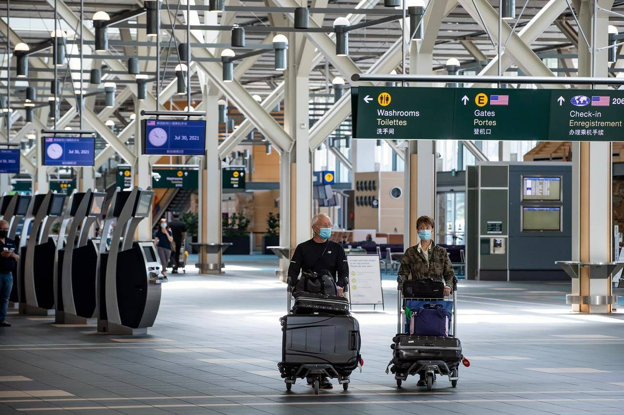 Travellers pushing luggage on carts walk through Vancouver International Airport, in Richmond, B.C., on Friday, July 30, 2021. By early next week, Canadians and all other foreign visitors who travel to the United States by air will need to get a COVID-19 test no later than the day before their departure.THE CANADIAN PRESS/Darryl Dyck