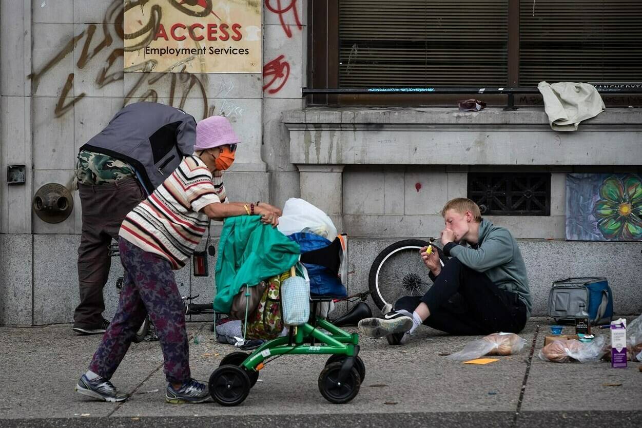 A woman walks past a person using a glass pipe to smoke drugs in the Downtown Eastside of Vancouver, on International Overdose Awareness Day on Tuesday, August 31, 2021. Researchers in British Columbia say the expansion of overdose prevention sites in Vancouver led to immediate behaviour changes among some drug users as they entered addiction treatment, decreased the number of times they injected substances in public and shared syringes. THE CANADIAN PRESS/Darryl Dyck