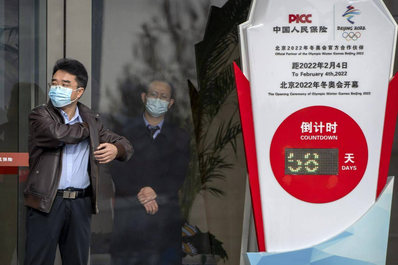 People wearing face masks stand near a clock outside of an office building counting down the days to the opening ceremony of the 2022 Winter Olympics in Beijing, Wednesday, Dec. 8, 2021. THE CANADIAN PRESS/AP, Mark Schiefelbein