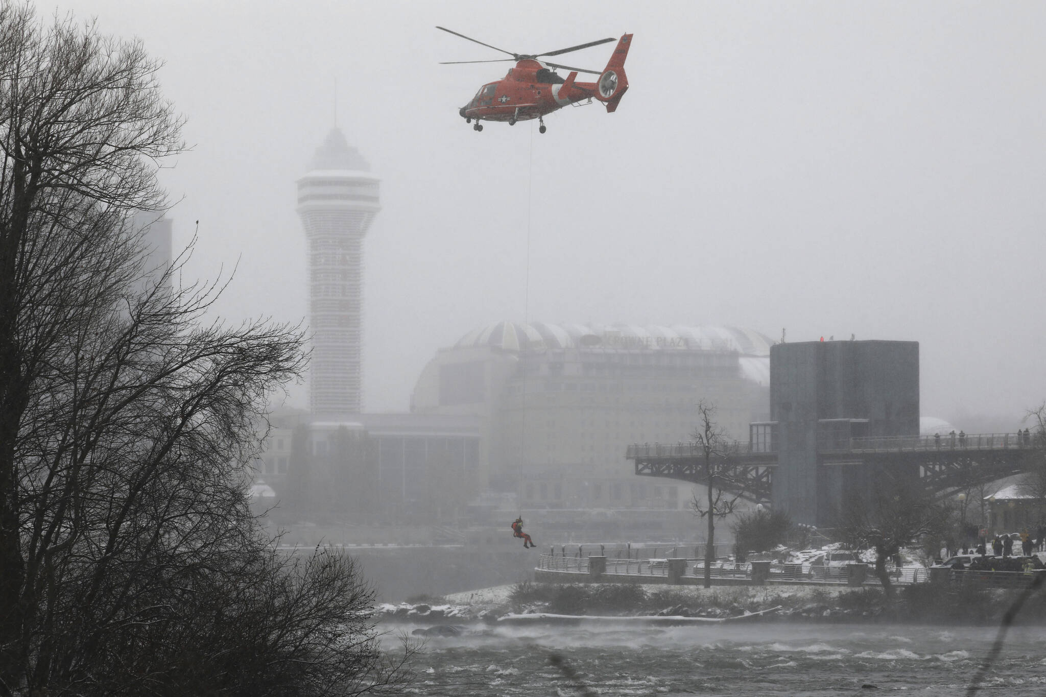 A U.S. Coast Guard rescue diver is lowered toward the vehicle lodged in the water at the brink of Niagara Falls, Wednesday, Dec. 8, 2021. (Derek Gee/Buffalo News via AP)