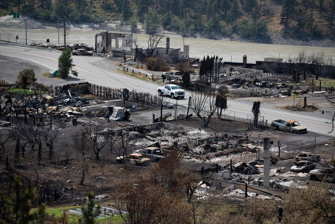 An RCMP vehicle drives past the remains of vehicles and structures in Lytton, B.C., on Friday, July 9, 2021, after a wildfire destroyed most of the village on June 30. The British Columbia government says it is immediately providing a grant of $1 million to support the Village of Lytton as it recovers from a destructive wildfire last summer. THE CANADIAN PRESS/Darryl Dyck