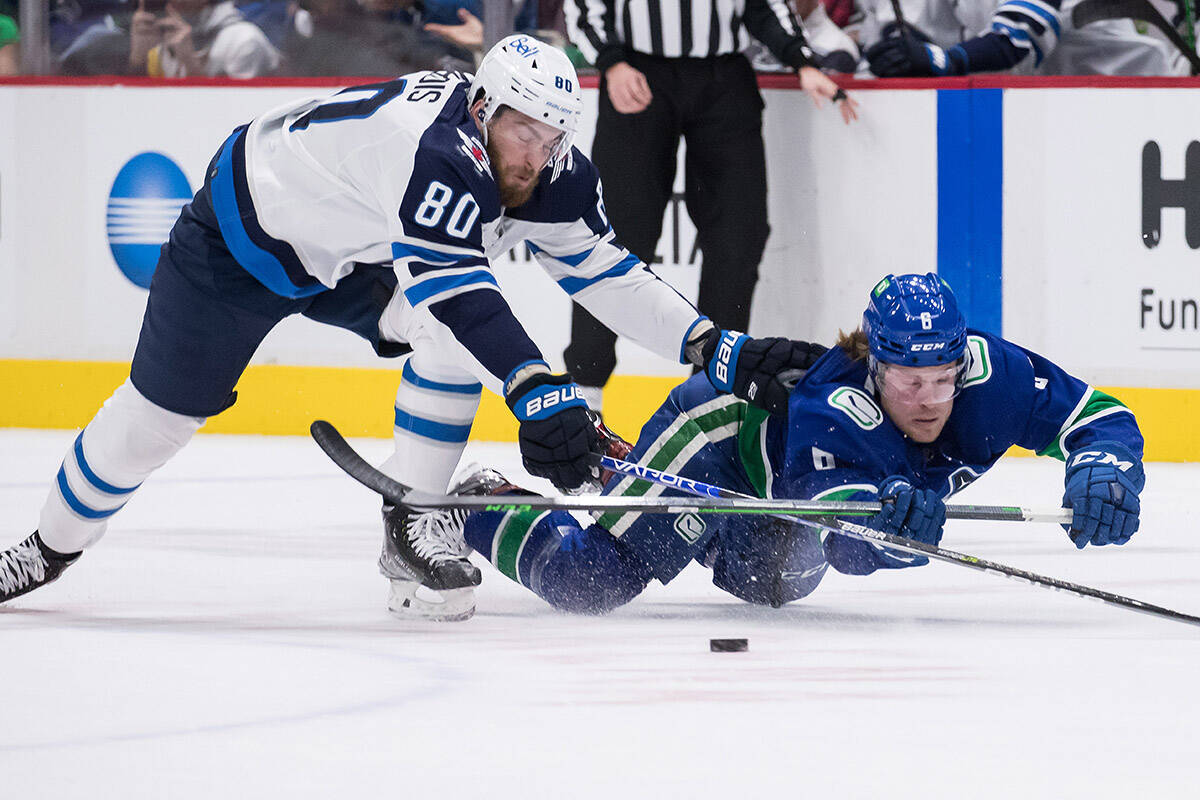 Vancouver Canucks’ Brock Boeser (6) dives to swat the puck away from Winnipeg Jets’ Pierre-Luc Dubois (80) during the first period of an NHL hockey game in Vancouver, on Friday, December 10, 2021. THE CANADIAN PRESS/Darryl Dyck