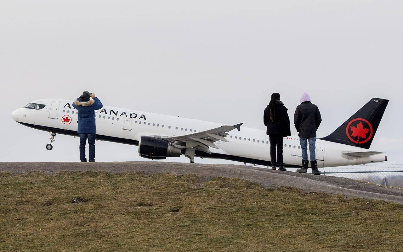 People look on as an Air Canada plane takes off from Montreal Trudeau Airport in Montreal, Sunday, Dec. 5, 2021. Confusion is the defining state for many Canadians contemplating travel this month amid shifting advice, COVID-19 variants and layers of testing and quarantine rules. THE CANADIAN PRESS/Graham Hughes
