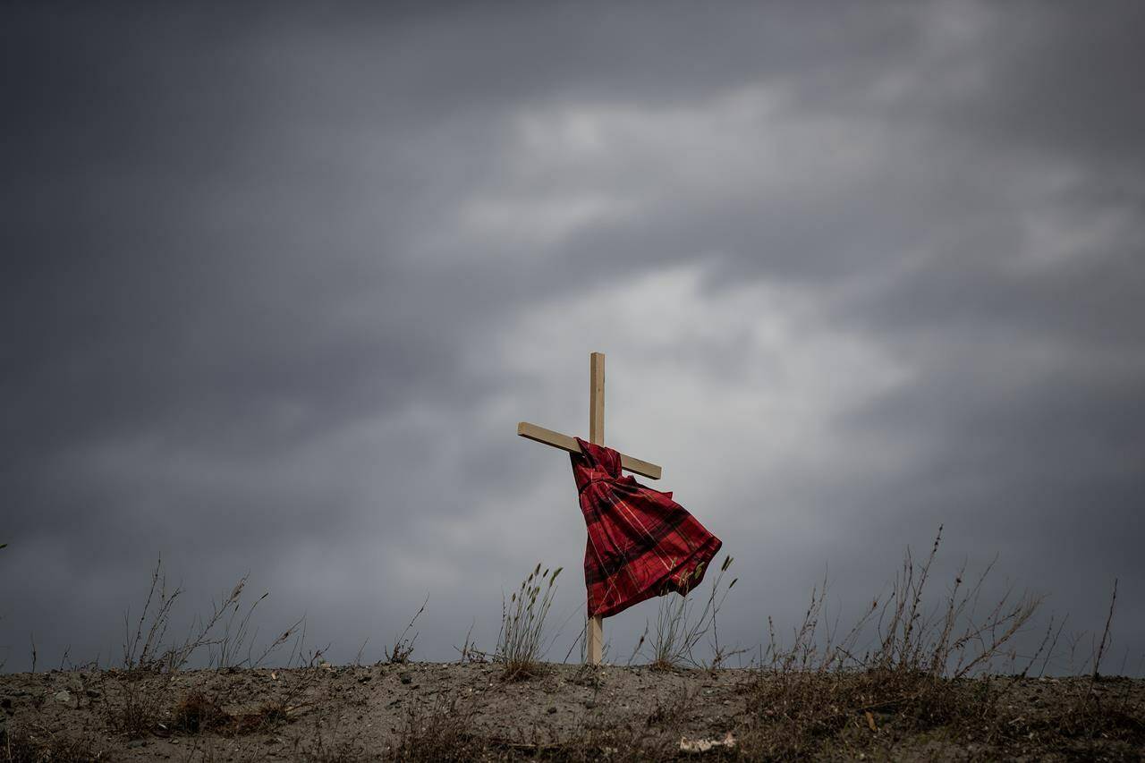 A child’s dress hung on a cross blows in the wind near the former Kamloops Indian Residential School to honour the 215 children whose remains are believed to have been discovered buried near the facility in Kamloops, B.C., on Friday, June 4, 2021. THE CANADIAN PRESS/Darryl Dyck