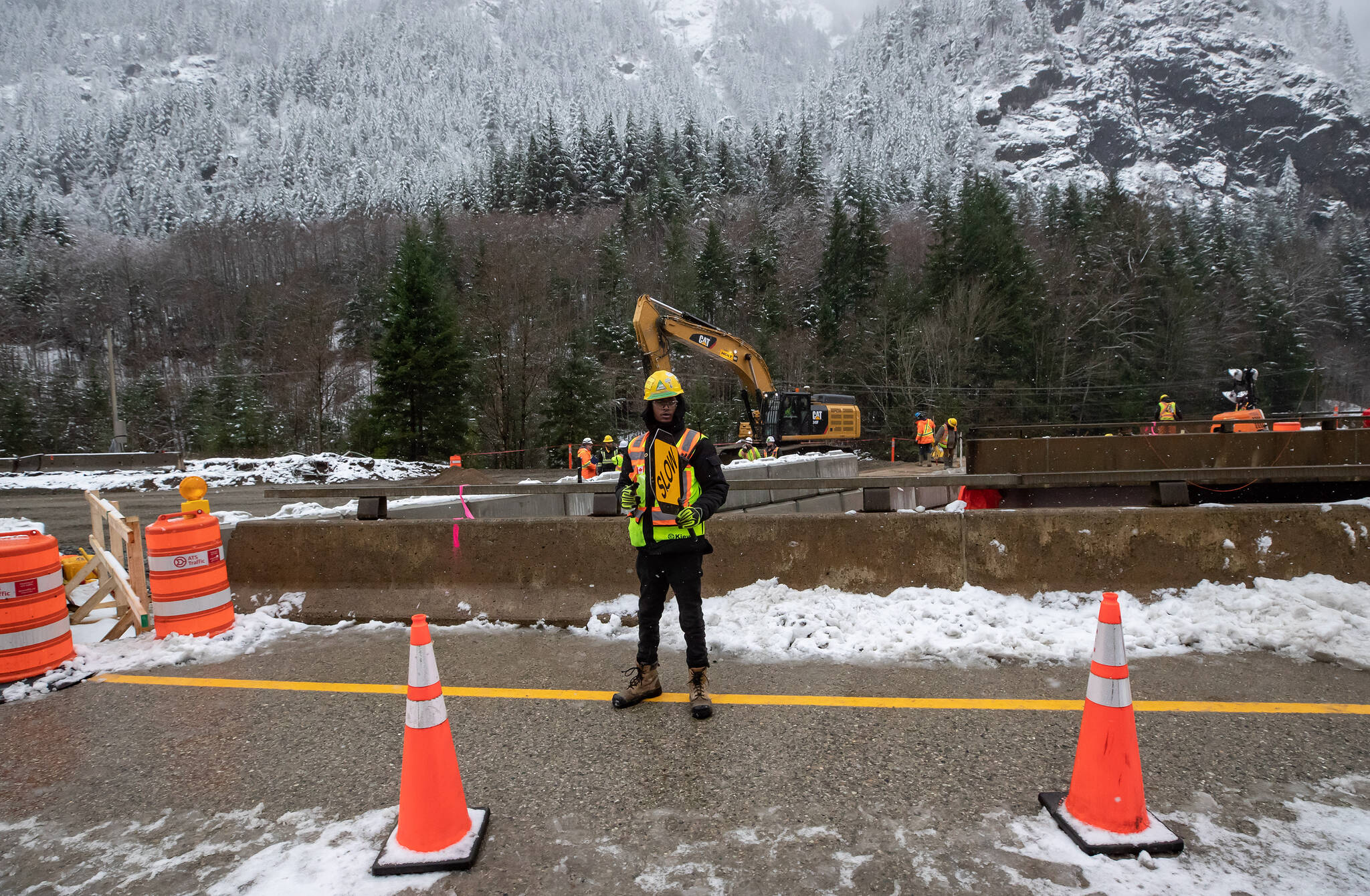 A flagger directs construction traffic while heavy equipment is used as repairs to a bridge and road that was washed out by flooding are underway on the Coquihalla Highway near Carolin Mine Road, northeast of Hope, B.C., Friday, Dec. 10, 2021. According to the B.C. Transportation Ministry the highway, which was heavily damaged in numerous places during last month’s flooding and mudslides, is on track to reopen to essential travel in early January if weather cooperates. THE CANADIAN PRESS/Darryl Dyck