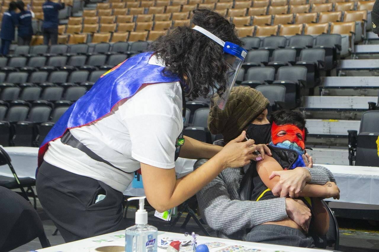 Six-year-old Jaiden Kulkarni sits in the arms of his mother Neha as he receives his COVID-19 vaccine shot from his aunt Dr. Chetana Kulkarni from Sick Kids Hospital at a children’s vaccine clinic held at the Scotiabank Arena, in Toronto, on Sunday, Dec. 12, 2021.THE CANADIAN PRESS/Chris Young