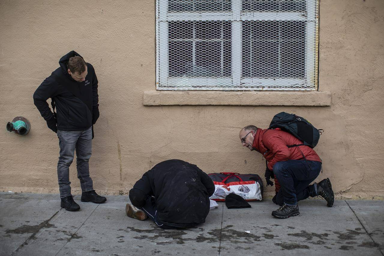 Manager of H.E.L.P. Team Boyle Street Community Services Doug Cooke, right, and outreach and support services manager Jared Tkachuk, left, check on a homeless person’s well-being in Edmonton on Thursday, Dec. 9, 2021. THE CANADIAN PRESS/Jason Franson