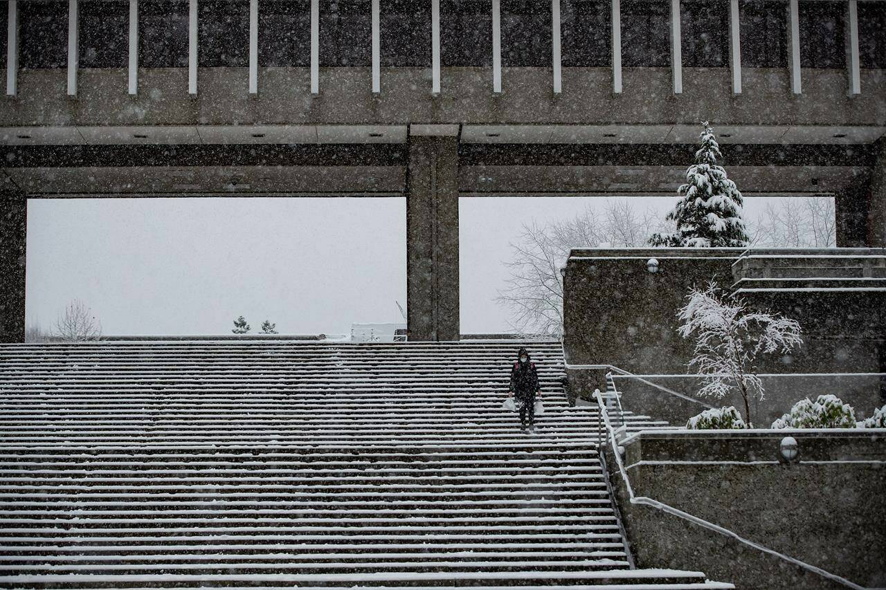 A woman wearing a face mask to curb the spread of COVID-19 walks down steps on the Simon Fraser University campus, as heavy snow falls in Burnaby, B.C., on Monday, December 21, 2020. THE CANADIAN PRESS/Darryl Dyck