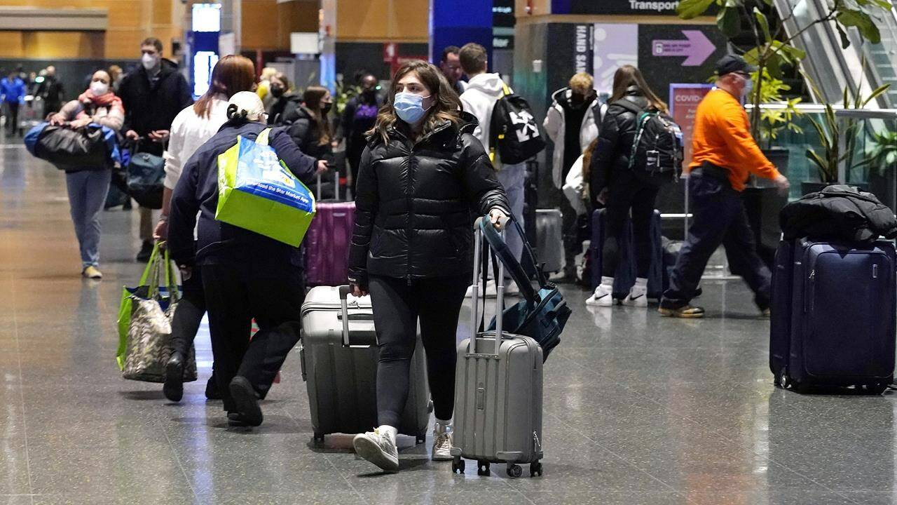 Travelers trek through Terminal E at Logan Airport, Tuesday, Dec. 21, 2021, in Boston. At least three major airlines say they have canceled dozens of flights, Friday, Dec. 24, because illnesses largely tied to the omicron variant of COVID-19 have taken a toll on flight crew numbers during the busy holiday travel season. (AP Photo/Charles Krupa)