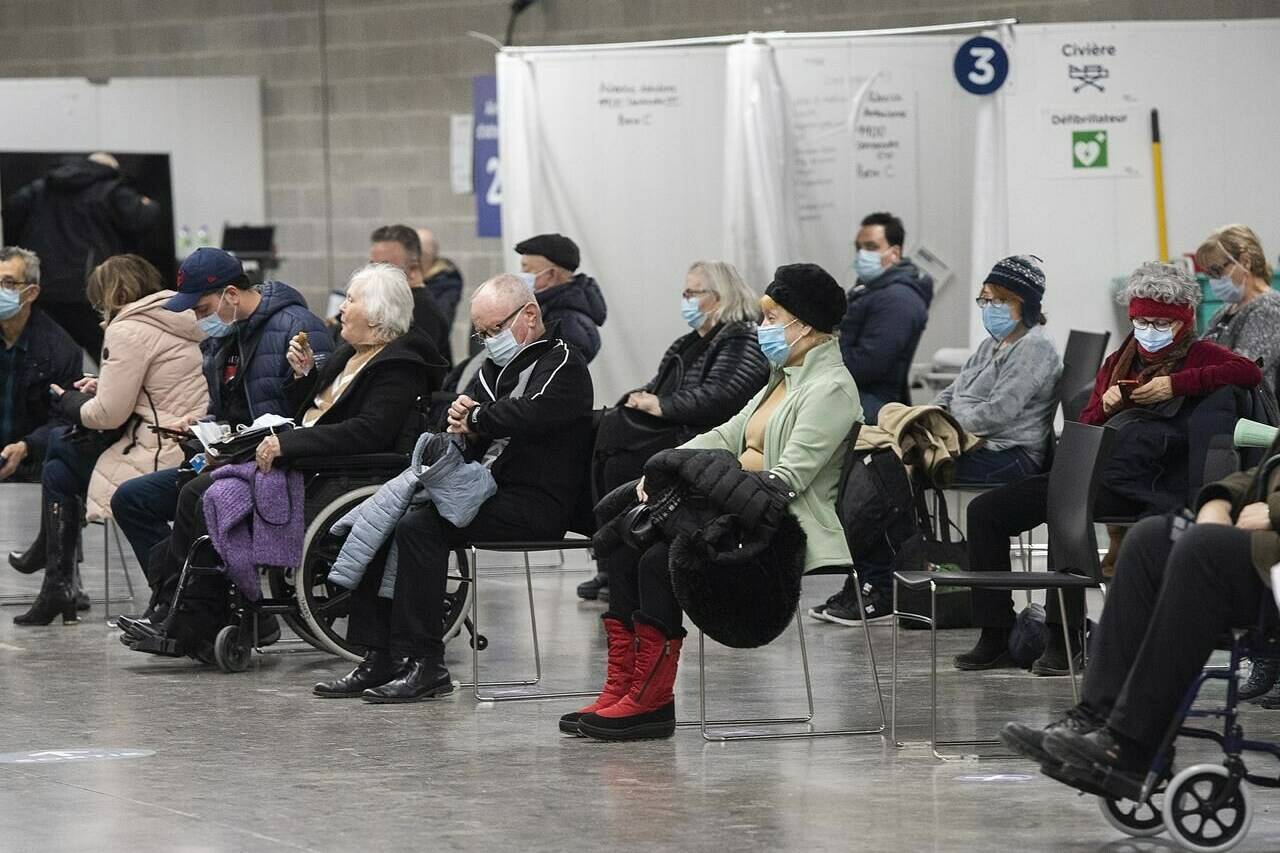 People wait to receive a COVID-19 booster vaccine dose at the Olympic Stadium in Montreal, Monday, Dec. 27, 2021. THE CANADIAN PRESS/Graham Hughes