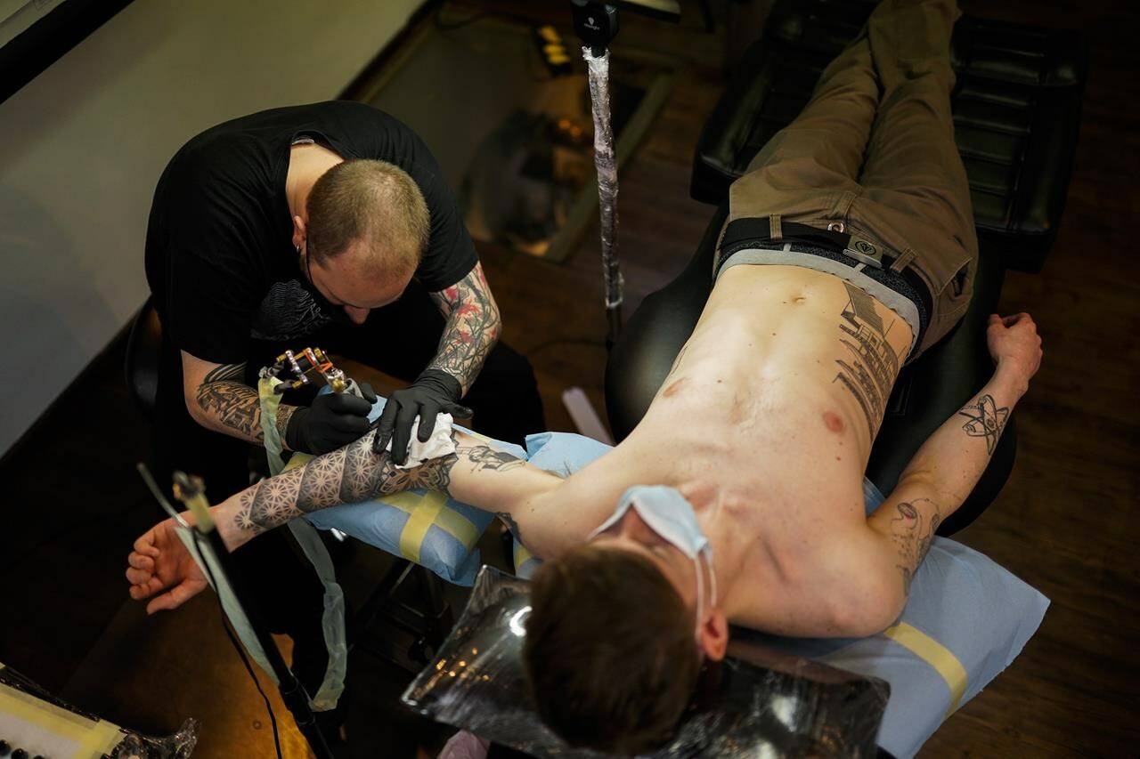 FILE - A man, wearing a protective face mask to prevent the spread of coronavirus, is tattooed at Paul and Friends tattoo parlour in downtown Brussels, March 26, 2021. The European Union is imposing restrictions on the inks that tattoo artists can use as of Wednesday, Jan. 5, 2022. The EU says it is a necessary move to protect the health of consumers because thousands of chemical elements now in use can cause anything from allergic reactions to cancer. The tattoo industry complains it is unfairly targeted and is losing an essence part of its art. (AP Photo/Francisco Seco, File)