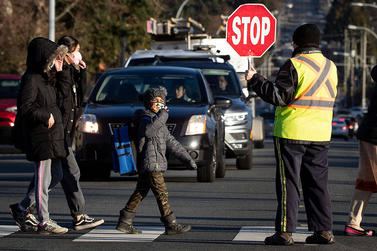 A crossing guard stops traffic as students wearing face masks to curb the spread of COVID-19 arrive at Ecole Woodward Hill Elementary School, in Surrey, B.C., on Tuesday, February 23, 2021. THE CANADIAN PRESS/Darryl Dyck