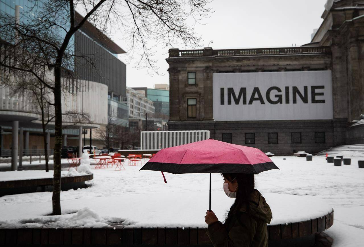 A person wearing a face mask carries an umbrella as rain falls while walking past the snow-covered square outside the Vancouver Art Gallery in Vancouver, on Thursday, January 6, 2022. The agency that monitors British Columbia’s waterways is warning of “minor to significant flooding” on B.C.’s Lower Mainland and Vancouver Island as warming temperatures and persistent rain melt heavy snow. THE CANADIAN PRESS/Darryl Dyck