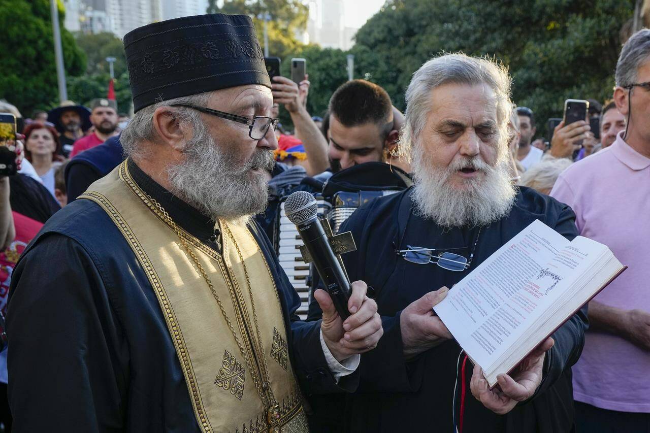 Serbian priests hold a service for Novak Djokovic and his supporters outside the Park Hotel, used as an immigration detention hotel where Djokovic is confined in Melbourne, Australia, Sunday, Jan. 9, 2022. After four nights in hotel detention Novak Djokovic will get his day in court on Monday in a controversial immigration case that has polarized opinions in the tennis world and elicited heartfelt support for the star back home in his native Serbia. (AP Photo/Mark Baker)