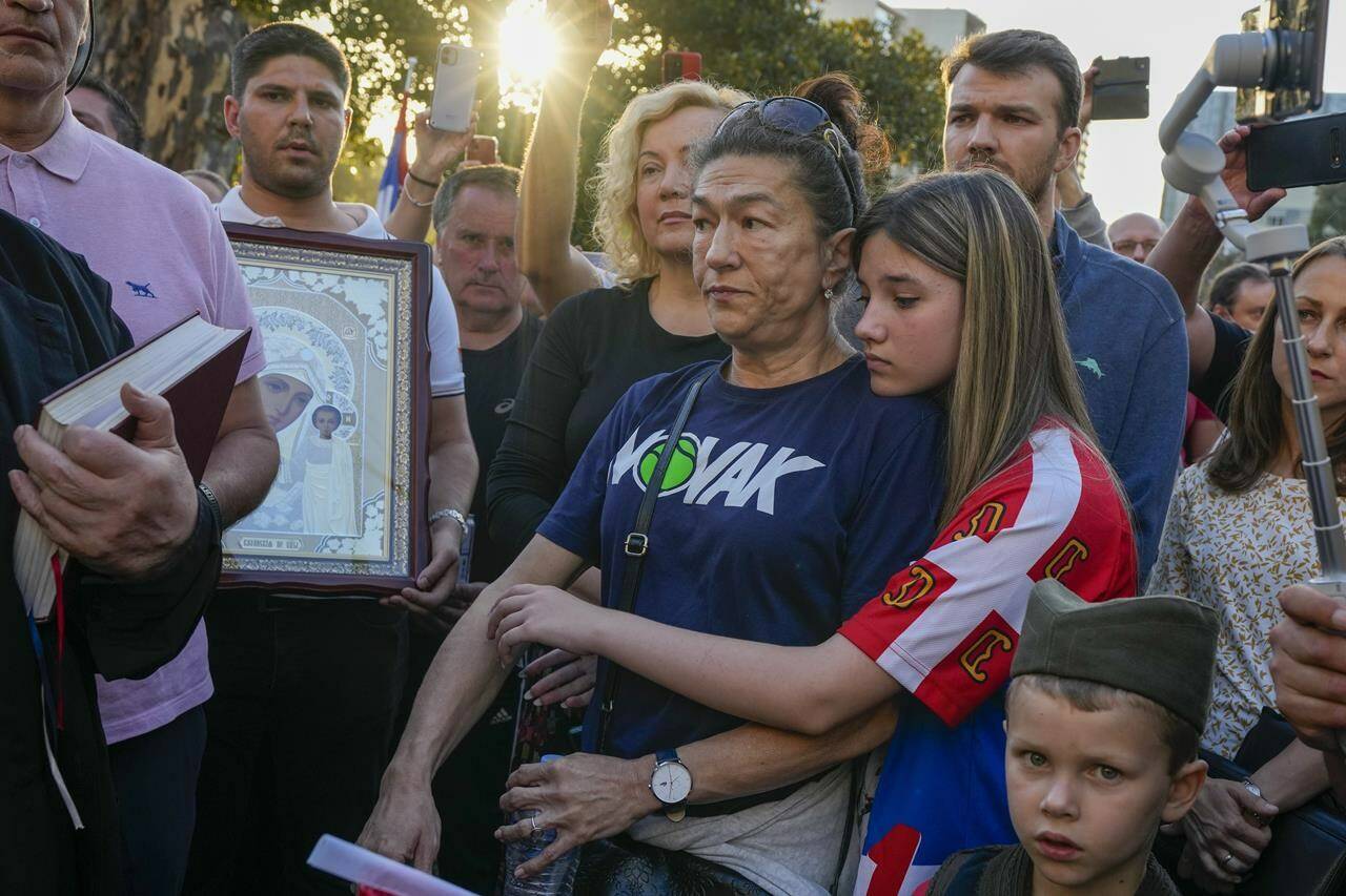 A young girl embraces her mother as Serbian priests hold a service for Novak Djokovic and his supporters outside the Park Hotel, used as an immigration detention hotel where Djokovic is confined in Melbourne, Australia, Sunday, Jan. 9, 2022. After four nights in hotel detention Novak Djokovic will get his day in court on Monday in a controversial immigration case that has polarized opinions in the tennis world and elicited heartfelt support for the star back home in his native Serbia. (AP Photo/Mark Baker)