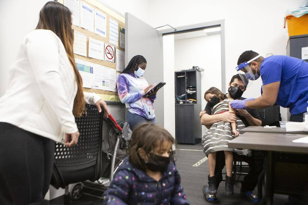 Seven-year-old Lorena Limdao is held by her father William as Dr. Kevin Evelyn of UHN gives her a COVID-19 vaccine needle while mother Gisella (left) looks on. They were at a “Kids and Families Vaccine Clinic” operated by Black Creek Community Health Centre in the Jane and Finch Mall in Toronto on Thursday, January 13, 2022. THE CANADIAN PRESS/Chris Young