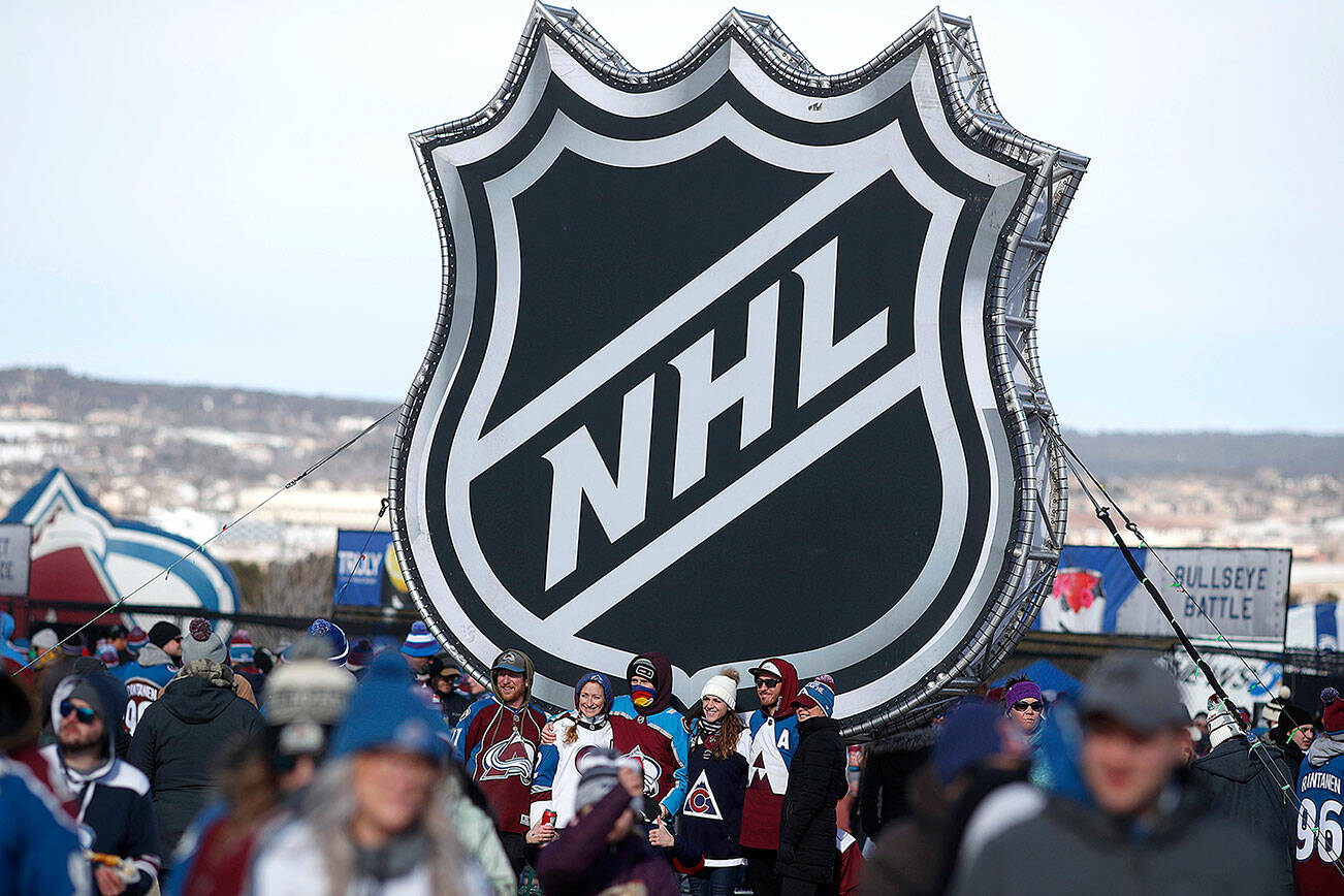 In this Saturday, Feb. 15, 2020, file photo, fans pose below the NHL league logo at a display outside Falcon Stadium before an NHL Stadium Series outdoor hockey game between the Los Angeles Kings and Colorado Avalanche, at Air Force Academy, Colo. (AP Photo/David Zalubowski, File)