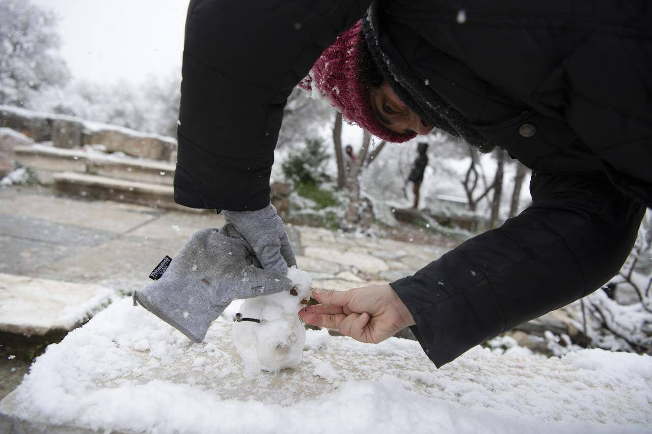 A woman makes a snow man during a snowfall, in Athens, on Monday, Jan. 24, 2022. A severe weather front has hit Greece, with sub-freezing temperatures and snowfall in many parts of the country, including the capital Athens and many Aegean islands.(AP Photo/Michael Varaklas)