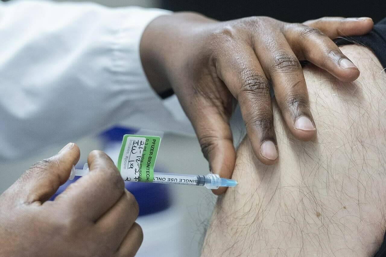 A man receives a Pfizer-BioNTech COVID-19 booster vaccine dose at the Olympic Stadium in Montreal, Monday, Dec. 27, 2021. A new survey suggests a widening gap between the pandemic views of people who have opted to get a COVID-19 vaccine booster and those who are holding steady with only two shots. THE CANADIAN PRESS/Graham Hughes