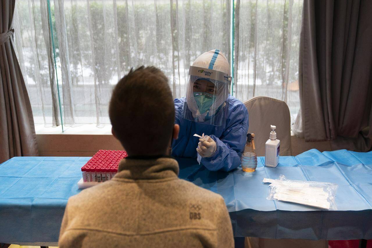 A medical worker in protective gear collects a swab sample from a video technician visiting from Belgium at a COVID-19 testing site set up inside a hotel at the 2022 Winter Olympics, Tuesday, Jan. 25, 2022, in Beijing. THE CANADIAN PRESS/AP/Jae C. Hong