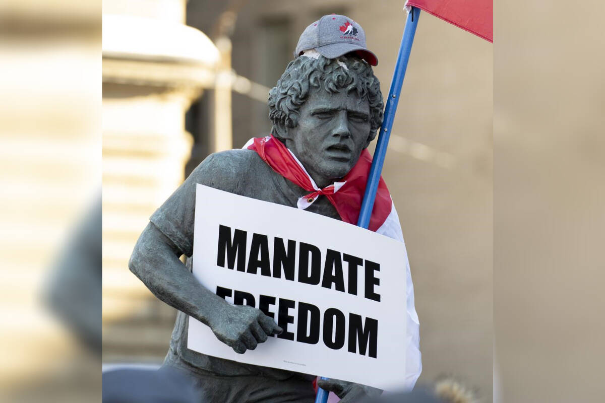 A statue of Terry Fox is decorated with a Canadian flag, protest sign and hat as protesters participating in a cross-country truck convoy protesting measures taken by authorities to curb the spread of COVID-19 and vaccine mandates gather on Parliament Hill in Ottawa, Saturday, Jan. 29, 2022. Some protesters jumped on the Tomb of the Unknown Soldier and others fastened an inverted Canadian flag to a statue of Terry Fox as they decried vaccine mandates in the nation’s capital on Saturday. THE CANADIAN PRESS/Adrian Wyld