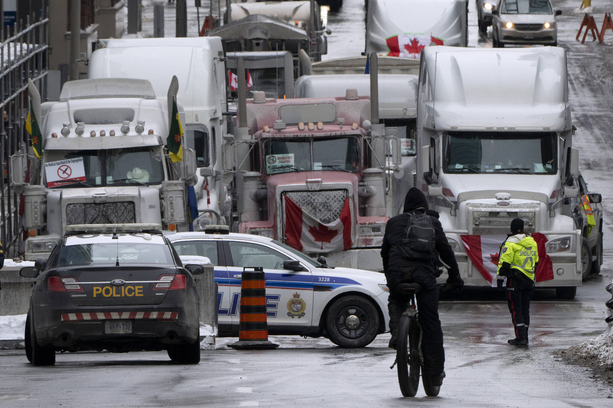 A cyclist rides towards a police barricade where trucks are lined up near Parliament hill on Wednesday, Feb. 2, 2022 in Ottawa. THE CANADIAN PRESS/Adrian Wyld