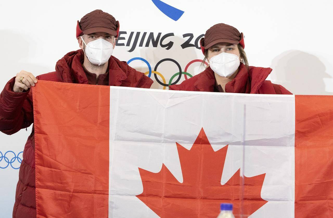 Speedskater Charles Hamelin, left, and hockey player Marie-Philip Poulin hold up the Canadian flag after being named as flag-bearers at a news conference Wednesday, February 2, 2022 at the 2022 Winter Olympics in Beijing. THE CANADIAN PRESS/Ryan Remiorz