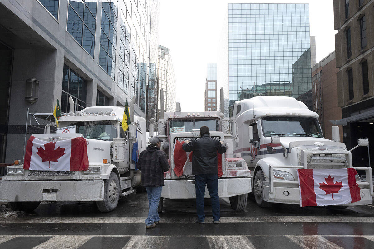 Truck drivers hang a Canadian flag on the front grill of a truck parked in downtown Ottawa near Parliament Hill on Wednesday, Feb. 2, 2022. THE CANADIAN PRESS/Adrian Wyld