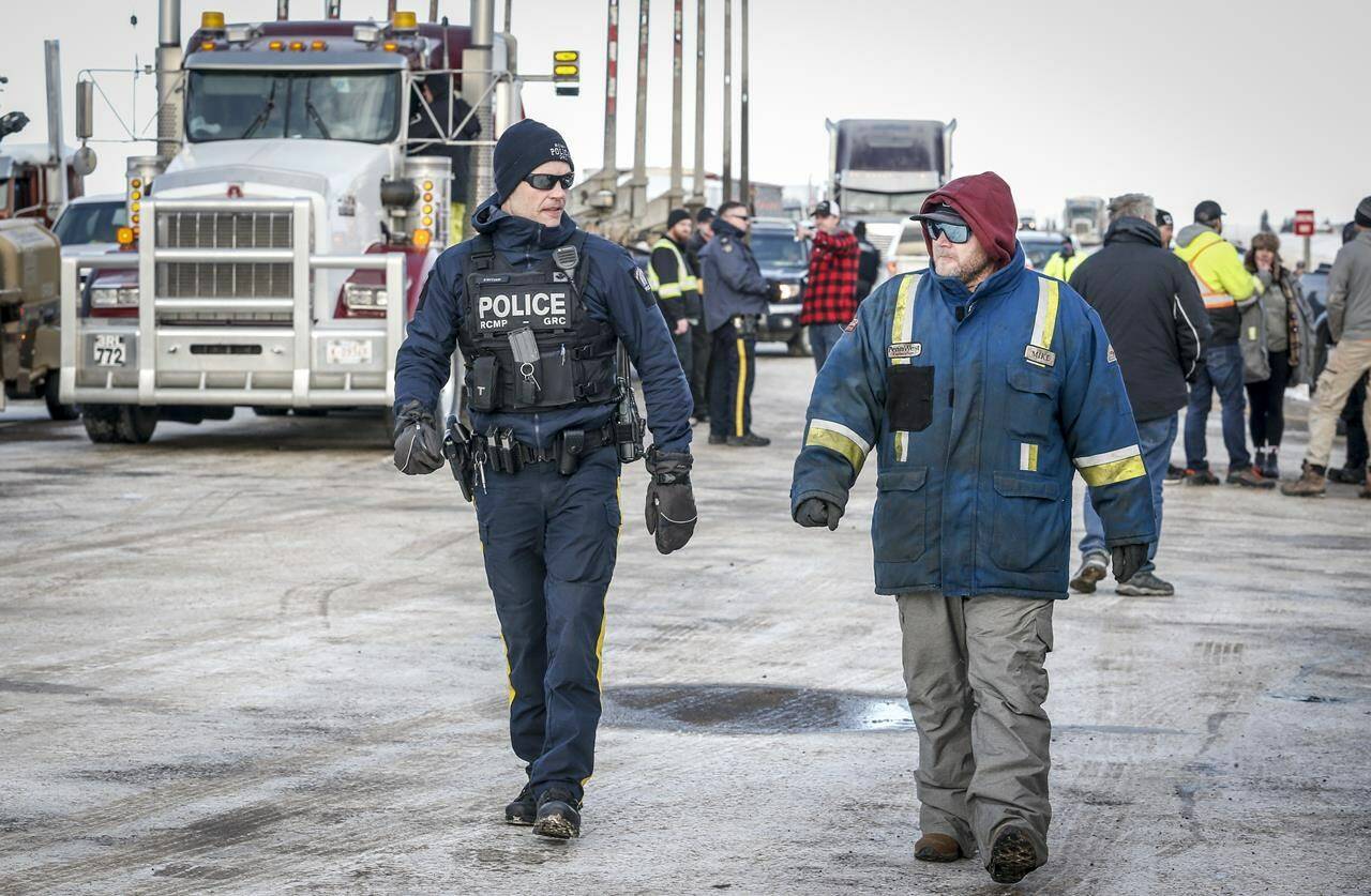 An RCMP officer talks with an anti-COVID-19 vaccine mandate demonstrator at road block on the highway in Milk River, Alta., Thursday, Feb. 3, 2022. THE CANADIAN PRESS/Jeff McIntosh