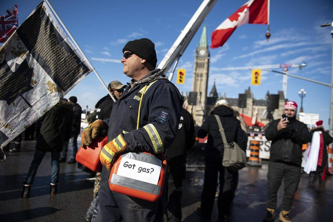 A protester carries fuel containers on Wellington Street, a day after police seized thousands of litres of fuel from an encampment in an attempt to quell a protest against COVID-19 restrictions that has been marked by gridlock and the sound of truck horns in Ottawa on Monday, Feb. 7, 2022. THE CANADIAN PRESS/Justin Tang