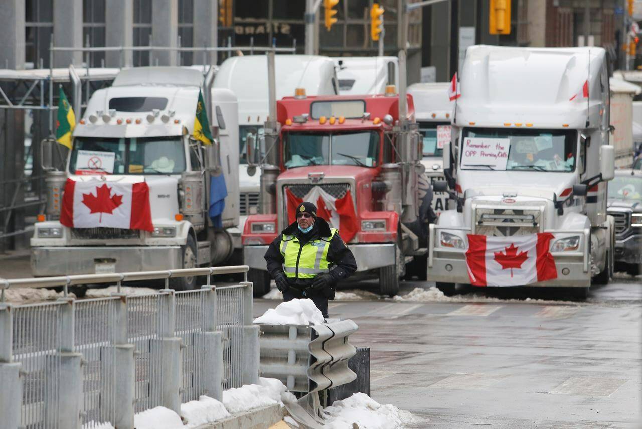 A police member stands in front of trucks blocking downtown streets as a rally against COVID-19 restrictions, which began as a cross-country convoy protesting a federal vaccine mandate for truckers, continues in Ottawa, on Wednesday, February 9, 2022. THE CANADIAN PRESS/ Patrick Doyle